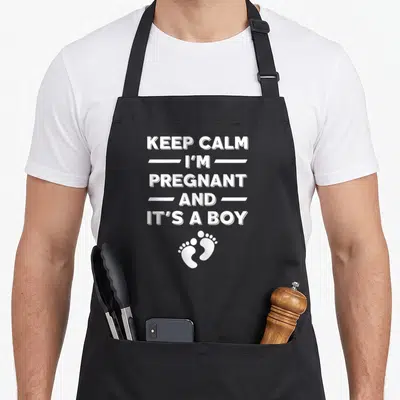 Tablier de cuisine noir avec l'inscription Keep calm I'm pregnant and it's a boy surplombant deux petits pieds blancs.