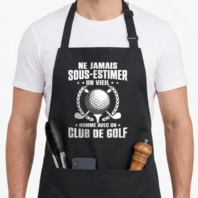 Tablier de cuisine noir avec une balle de golf, deux clubs croisés et texte humoristique en blanc.