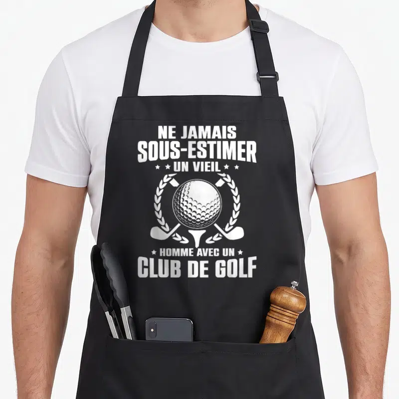 Tablier de cuisine noir avec une balle de golf, deux clubs croisés et texte humoristique en blanc.