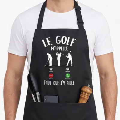 Tablier de cuisine noir avec l'inscription Le Golf m'appelle et trois silhouettes de joueurs en action au milieu du design.