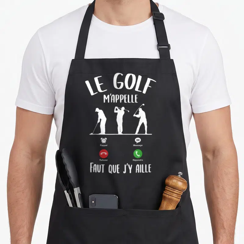 Tablier de cuisine noir avec l'inscription Le Golf m'appelle et trois silhouettes de joueurs en action au milieu du design.