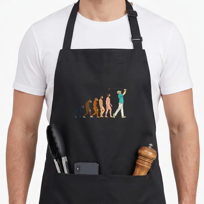 Tablier de cuisine noir avec illustration humoristique de l'évolution humaine se terminant par un golfeur en train de swinguer.
