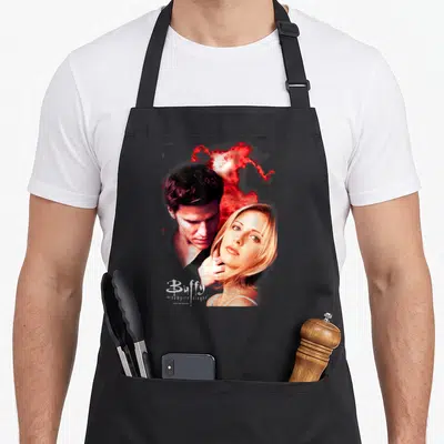 Tablier de cuisine noir avec illustration de Buffy et Angel sur fond de nuages rouges et logo blanc en bas à gauche.
