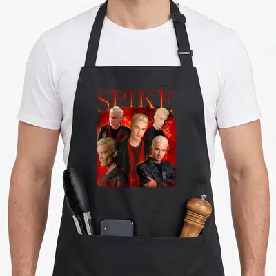 Tablier de cuisine noir avec un collage de portraits de Spike sur fond rouge et or, le nom SPIKE en lettres capitales oranges au sommet.