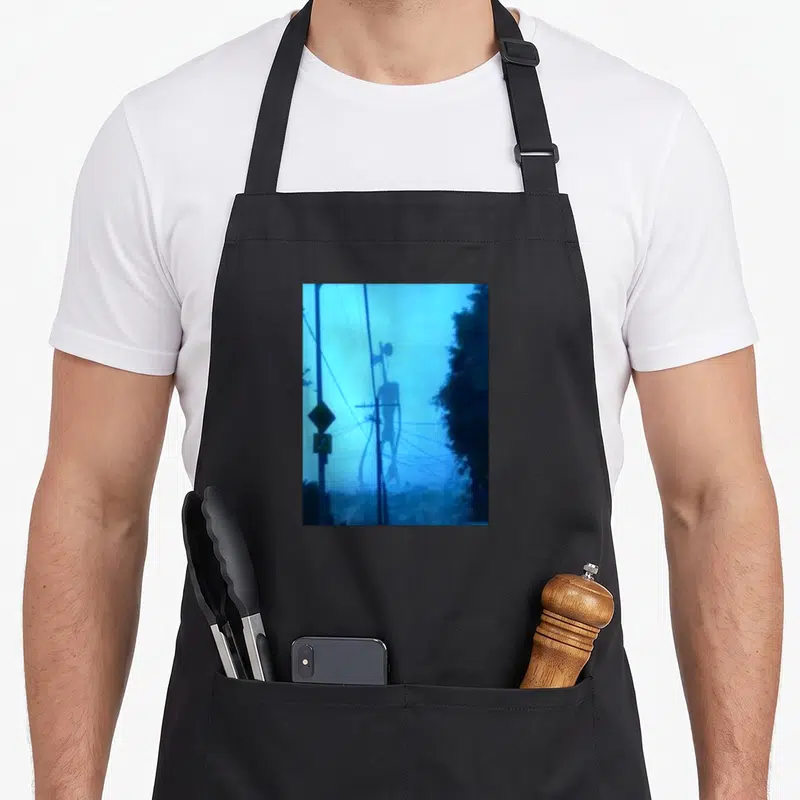 Tablier de cuisine noir avec une illustration bleutée représentant une haute silhouette aux têtes de sirène entre des fils électriques.