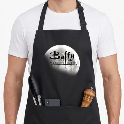 Tablier de cuisine noir avec une grande lune pleine et le titre stylisé en lettres noires au centre.