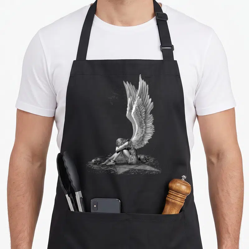 Tablier de cuisine noir avec illustration d'un ange enchaîné sur une étoile à cinq branches flanquée de crânes et de volutes décoratives.
