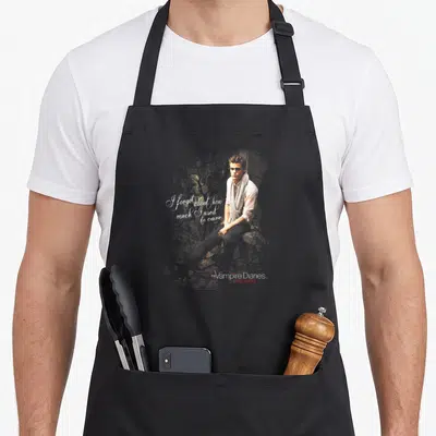 Tablier de cuisine noir avec illustration de Stefan et texte blanc calligraphié sur fond sombre texturé.
