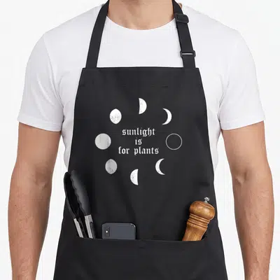 Tablier de cuisine noir avec texte sunlight is for plants et phases lunaires blanches en style grunge.