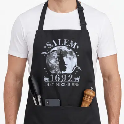 Tablier de cuisine noir avec silhouette sorcière pleine lune Salem 1692 chats et texte They missed one en blanc.