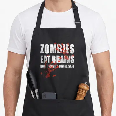 Tablier de cuisine noir avec inscription Zombies Eat Brains et éclaboussures rouges imitant du sang sur fond gris.