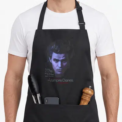 Tablier de cuisine noir avec portrait stylisé de Stefan Salvatore, citation en anglais et logo Love Sucks en bas à droite.