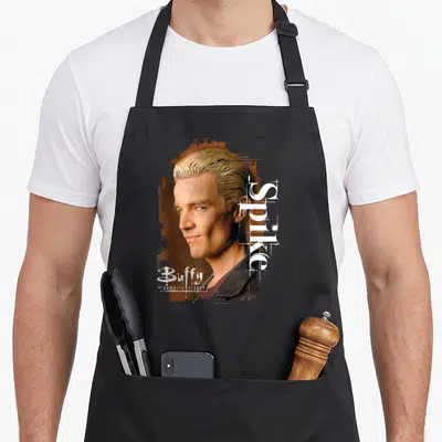 Tablier de cuisine noir avec portrait vintage de Spike et typographie blanche du titre Buffy le tueur de vampires sur fond orangé.