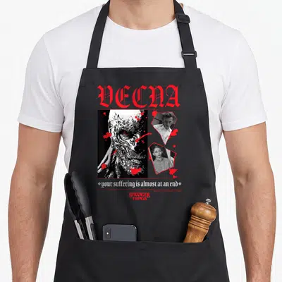 Tablier de cuisine noir avec illustration gothique rouge et blanche représentant Vecna et des portraits de Henry Creel encadrés de taches sanguinolentes.