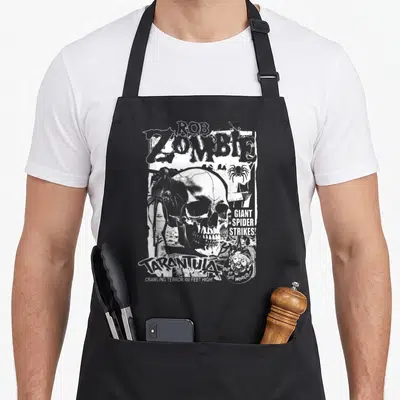 Tablier de cuisine noir avec illustration monochrome d'un crâne, d'une araignée et typographie horror vintage.