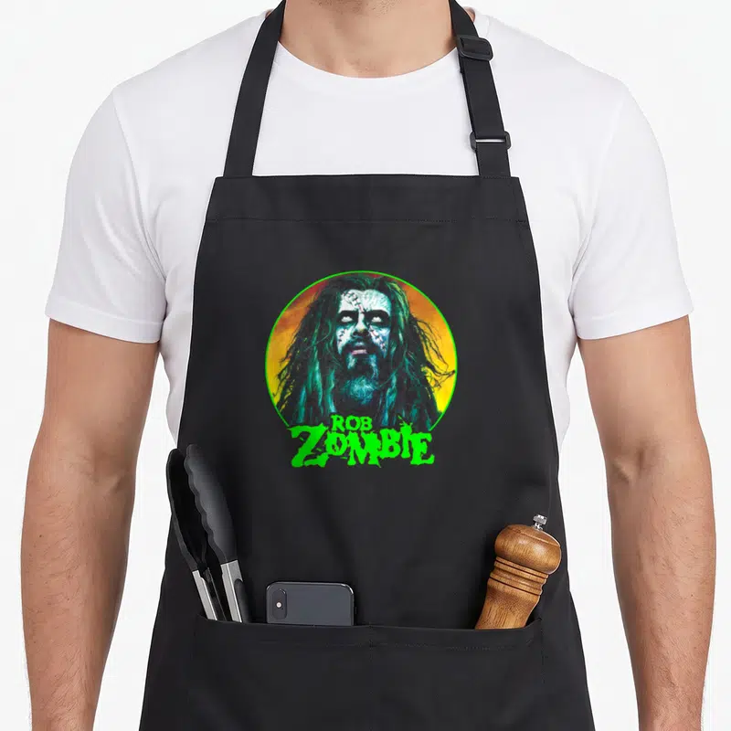 Tablier de cuisine noir avec illustration circulaire de Rob Zombie aux cheveux longs et texte vert fluorescent en dessous.