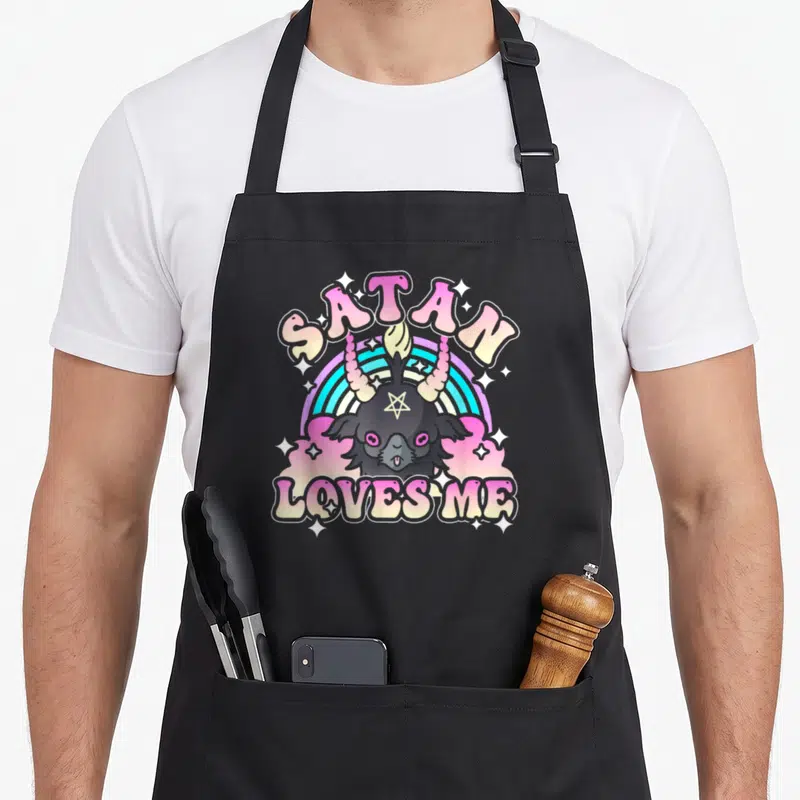 Tablier de cuisine noir avec tête de bouc pastel, arc-en-ciel et texte Satan Loves Me entouré d'étoiles scintillantes.