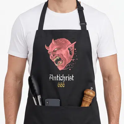Tablier de cuisine noir avec tête de diable rouge criant et texte Antichrist 666 en blanc et or.