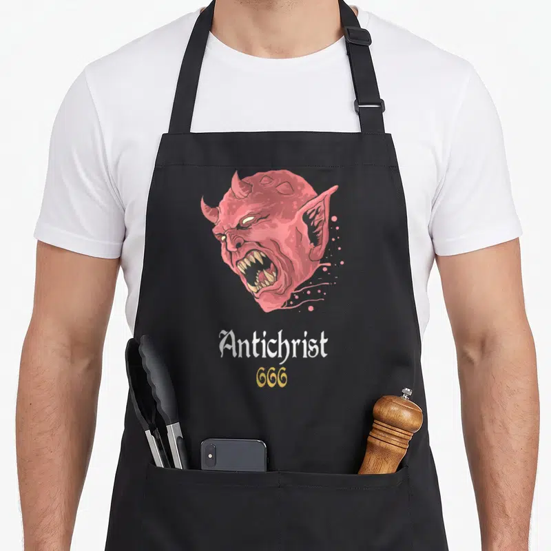 Tablier de cuisine noir avec tête de diable rouge criant et texte Antichrist 666 en blanc et or.