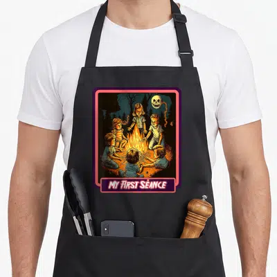 Tablier de cuisine noir avec illustration d'enfants autour d'un feu et un crâne flottant au-dessus.
