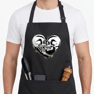 Tablier de cuisine noir avec deux crânes s'embrassant dans un cœur et texte Till Death Do Us Part