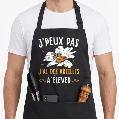 Tablier de cuisine noir avec inscription J'ai des abeilles à élever et dessin d'abeille sur une fleur blanche.