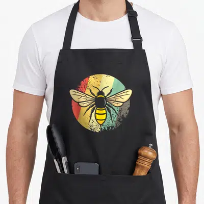 Tablier de cuisine noir avec une illustration circulaire d'abeille vintage sur fond multicolore rayé rouge jaune vert et beige.