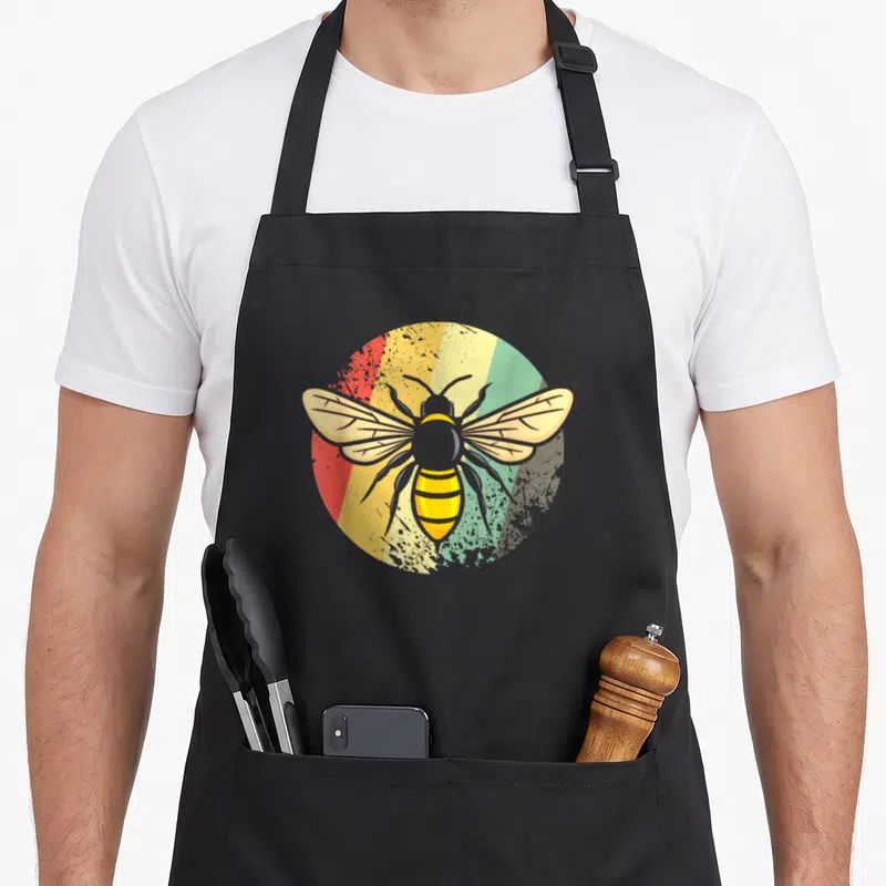 Tablier de cuisine noir avec une illustration circulaire d'abeille vintage sur fond multicolore rayé rouge jaune vert et beige.