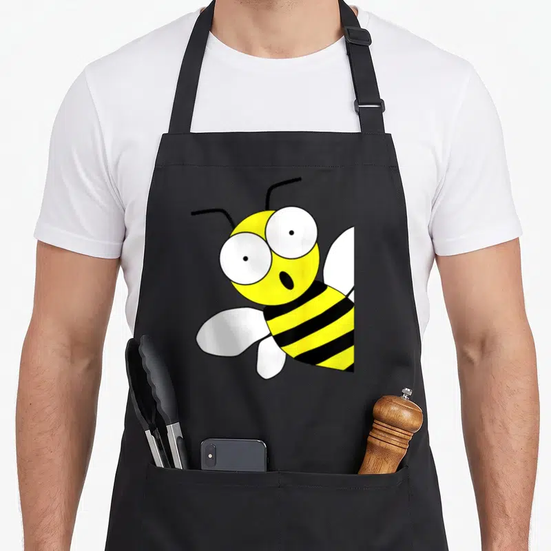 Tablier de cuisine noir avec illustration d'une abeille jaune aux grands yeux ronds et ailes blanches