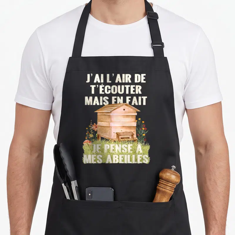 Tablier de cuisine noir avec une ruche en bois, des fleurs colorées et le texte J'ai l'air de t'écouter mais en fait je pense à mes abeilles.