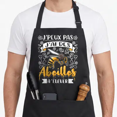 Tablier de cuisine noir avec inscription J'peux pas j'ai des Abeilles à élever et dessin d'abeille orange.