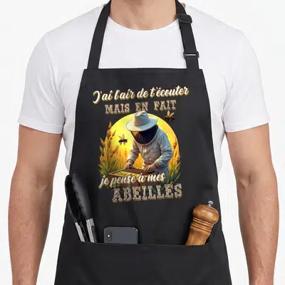 Tablier de cuisine noir avec illustration d'apiculteur et texte sur les abeilles dans un décor de soleil doré.