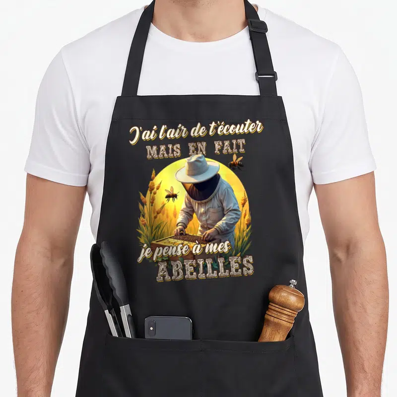 Tablier de cuisine noir avec illustration d'apiculteur et texte sur les abeilles dans un décor de soleil doré.