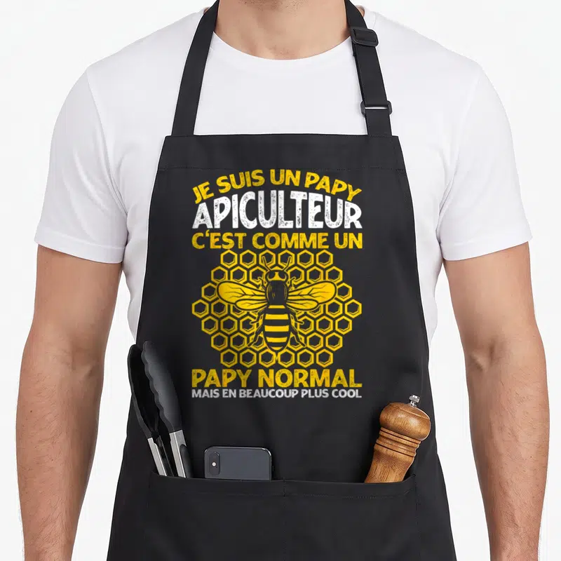 Tablier de cuisine noir avec illustration d'abeille et texte jaune blanc sur fond de ruche
