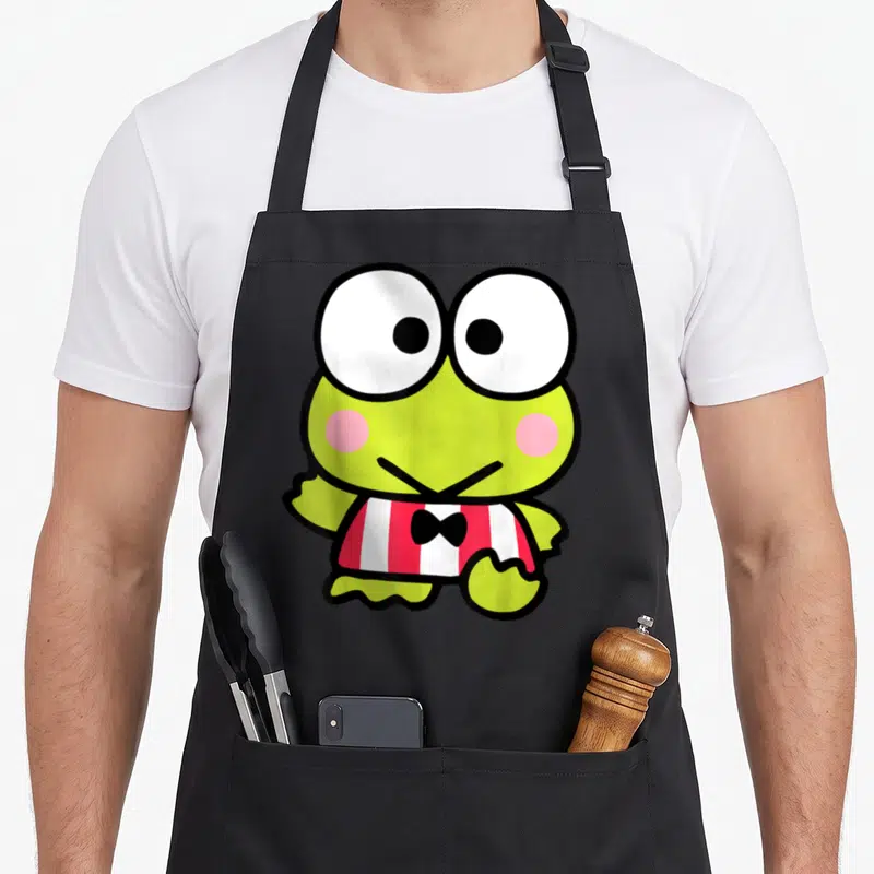 Tablier de cuisine noir avec illustration colorée d'une grenouille verte aux grands yeux blancs et vêtement rayé rouge et blanc.