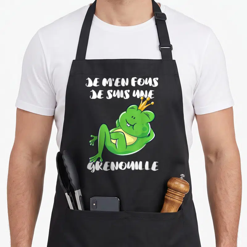 Tablier de cuisine noir avec une grenouille verte souriante portant une couronne dorée et le texte blanc Je m'en fous je suis une grenouille
