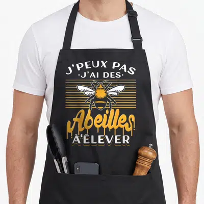 Tablier de cuisine noir avec une illustration d'abeille jaune et blanche et le texte J'peux pas j'ai des abeilles à élever.
