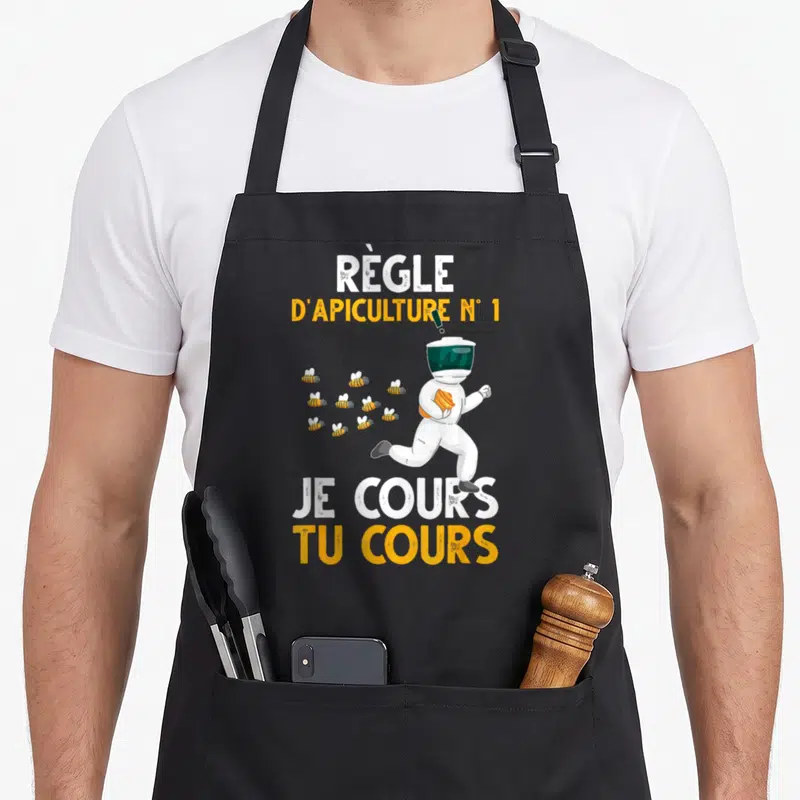 Tablier de cuisine noir avec un apiculteur en tenue blanche fuyant un vol d'abeilles jaunes et noires.