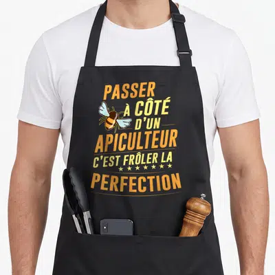 Tablier de cuisine noir avec inscription orange et jaune Passer à côté d'un apiculteur c'est frôler la perfection illustré par une abeille stylisée.
