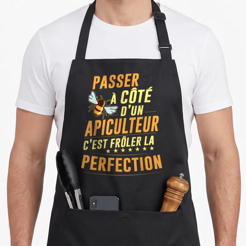 Tablier de cuisine noir avec inscription orange et jaune Passer à côté d'un apiculteur c'est frôler la perfection illustré par une abeille stylisée.