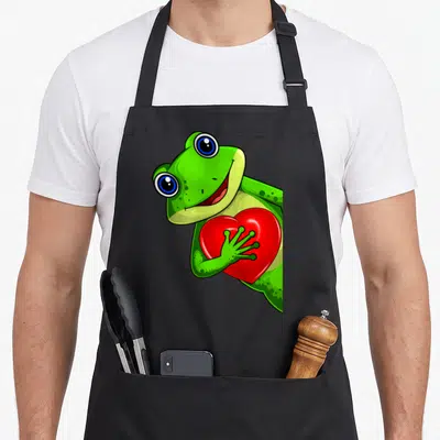 Tablier de cuisine noir avec une grenouille verte tenant un cœur rouge brillant, style cartoon expressif.