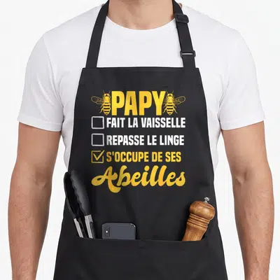 Tablier de cuisine noir avec l'inscription Papy s'occupe de ses abeilles et deux illustrations d'insectes jaunes.