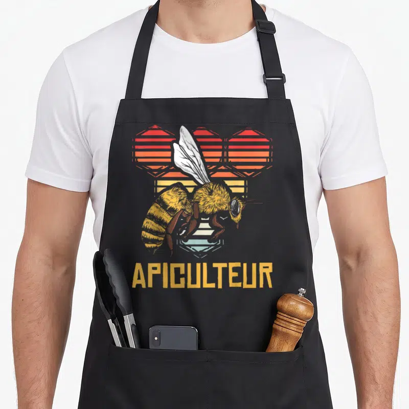 Tablier de cuisine noir avec une grande abeille jaune et le mot Apiculteur en lettres dorées sur fond géométrique orange.