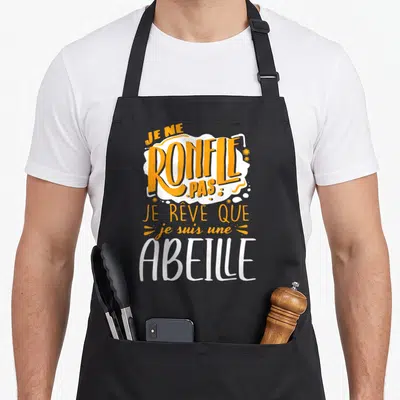 Tablier de cuisine noir avec le texte Je ne ronfle pas je rêve que je suis une abeille en orange et blanc.