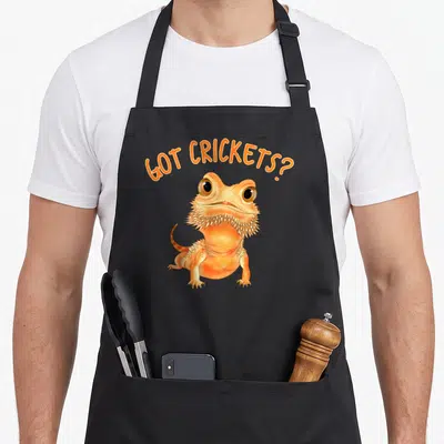 Tablier de cuisine noir avec illustration d'un dragon barbu orange et texte Got Crickets en arc.