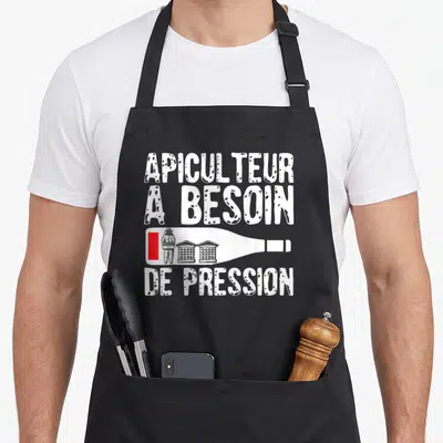 Tablier de cuisine noir avec l'inscription Apiculteur A Besoin De Pression et une illustration de bouteille contenant un apiculteur et des ruches.