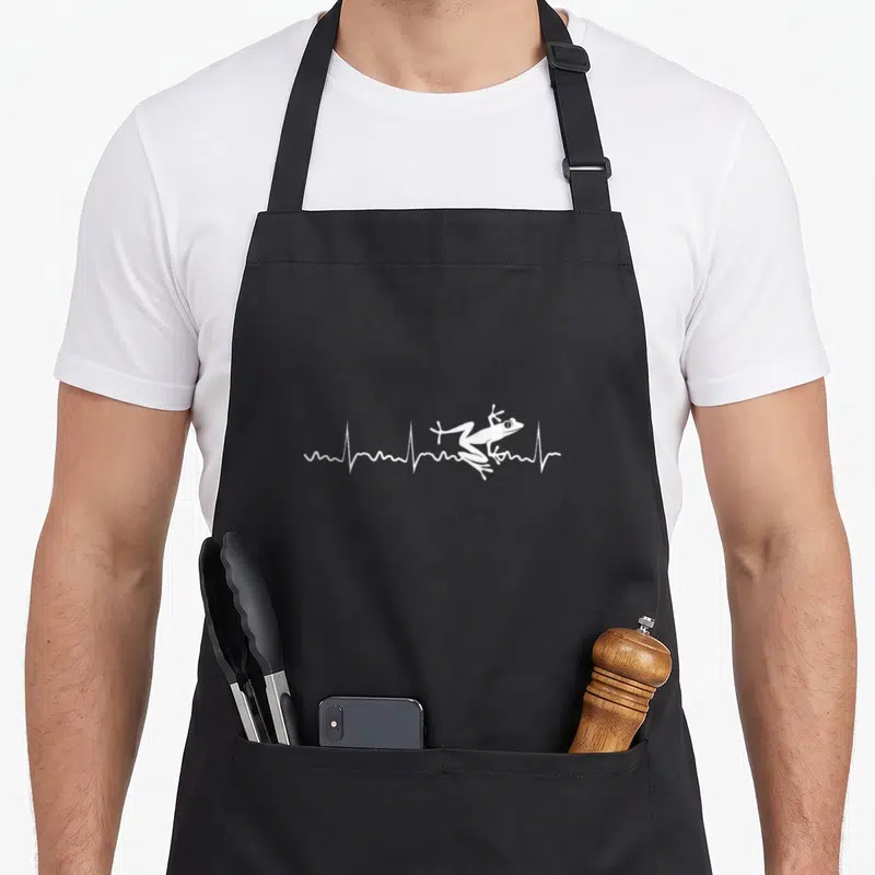 Tablier de cuisine noir avec une grenouille blanche sautant sur une ligne de rythme cardiaque stylisée.