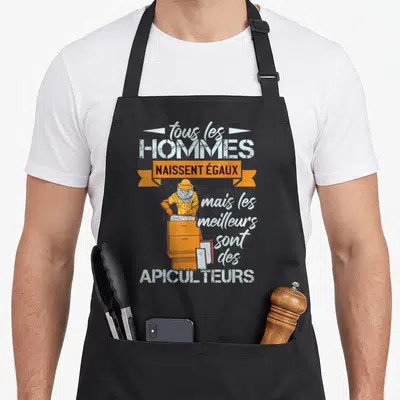 Tablier de cuisine noir avec illustration d'un apiculteur en tenue jaune manipulant une ruche orange et un message humoristique.