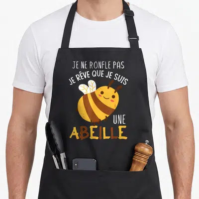 Tablier de cuisine noir avec une abeille jaune marron souriante et le texte blanc Je ne ronfle pas je rêve que je suis une abeille.