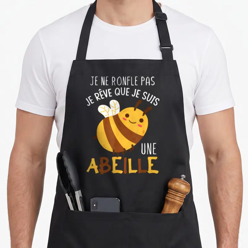 Tablier de cuisine noir avec une abeille jaune marron souriante et le texte blanc Je ne ronfle pas je rêve que je suis une abeille.
